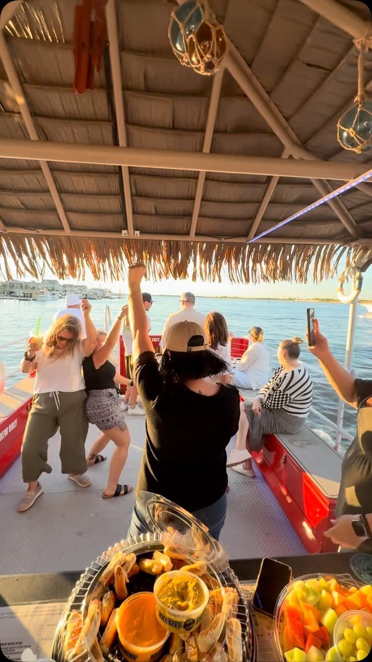 Group of adults celebrating on a red boat with shrimp and fruit platters.