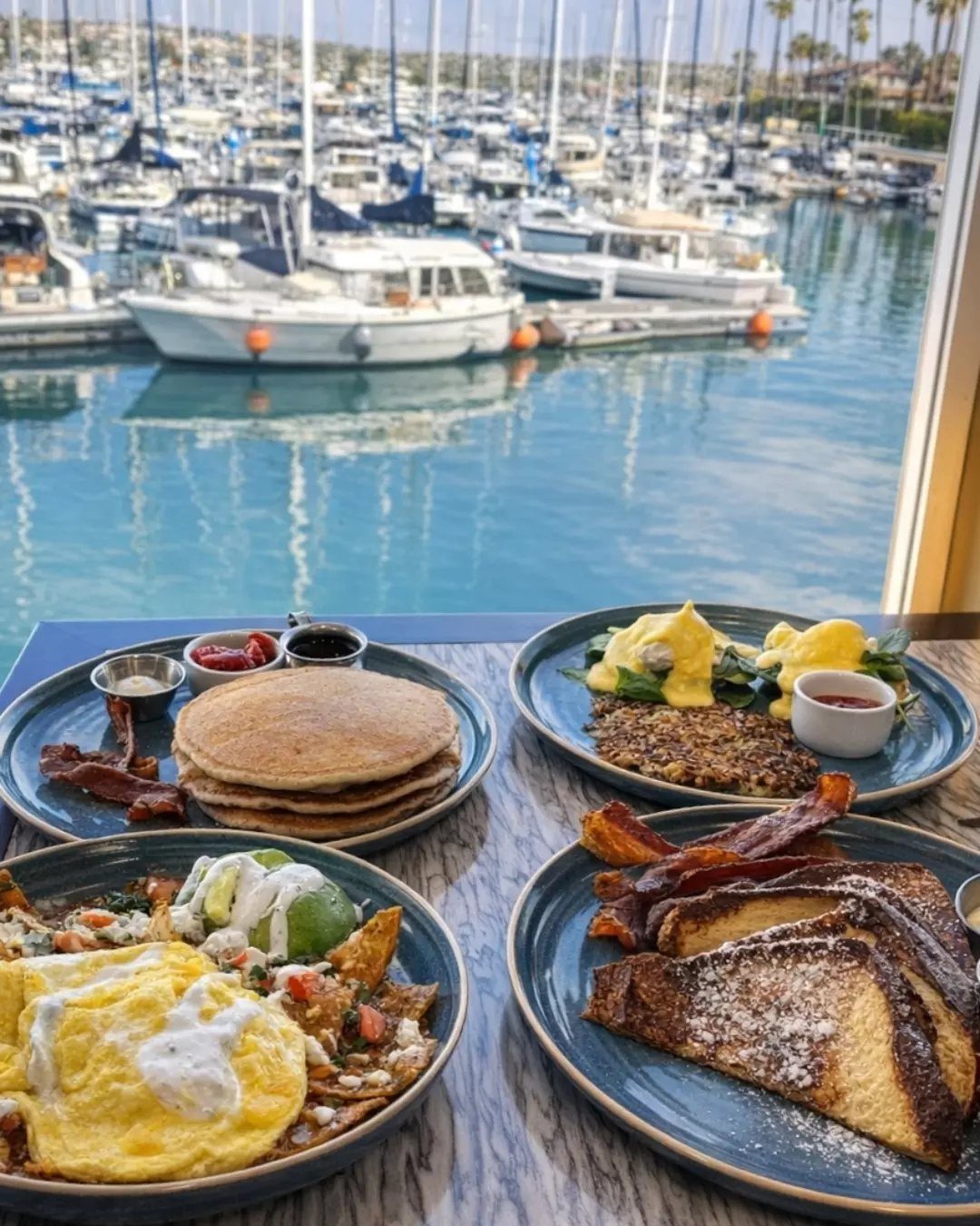Brunch plates with pancakes and eggs overlooking a marina filled with white boats.
