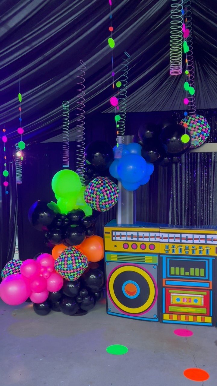 Colorful DJ booth and neon balloons in a dark party room with streamers.