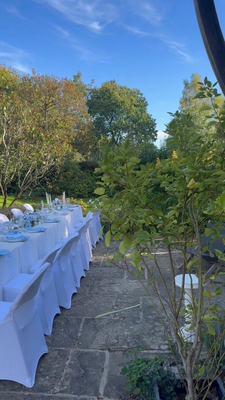 Long outdoor dining table with white linens and blue accents on a stone patio