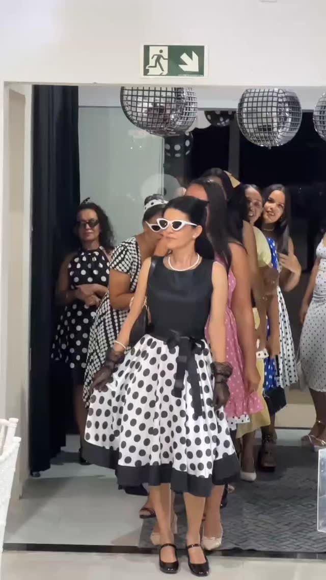 Women in vintage polka dot dresses and cat-eye sunglasses at a themed party.
