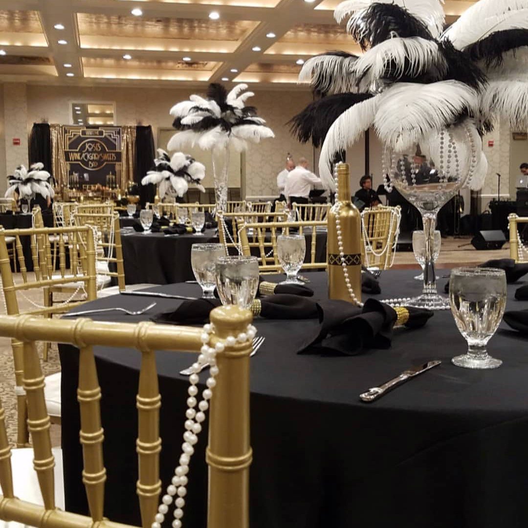 Black and gold banquet table settings with ostrich feather centerpieces and pearl accents.