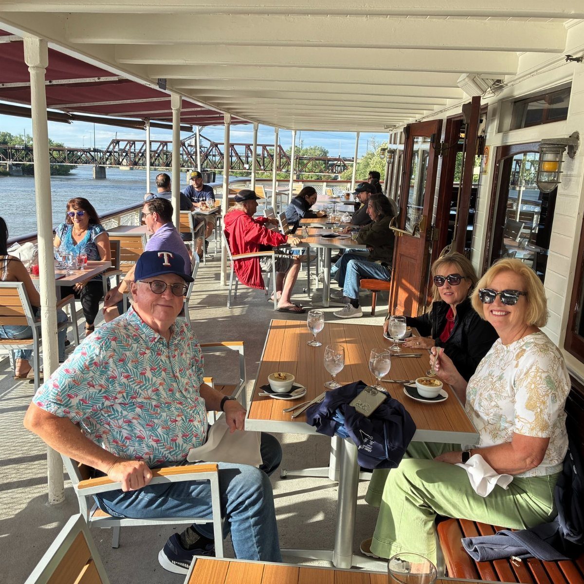 Older adults dining and socializing on the outdoor deck of a boat.
