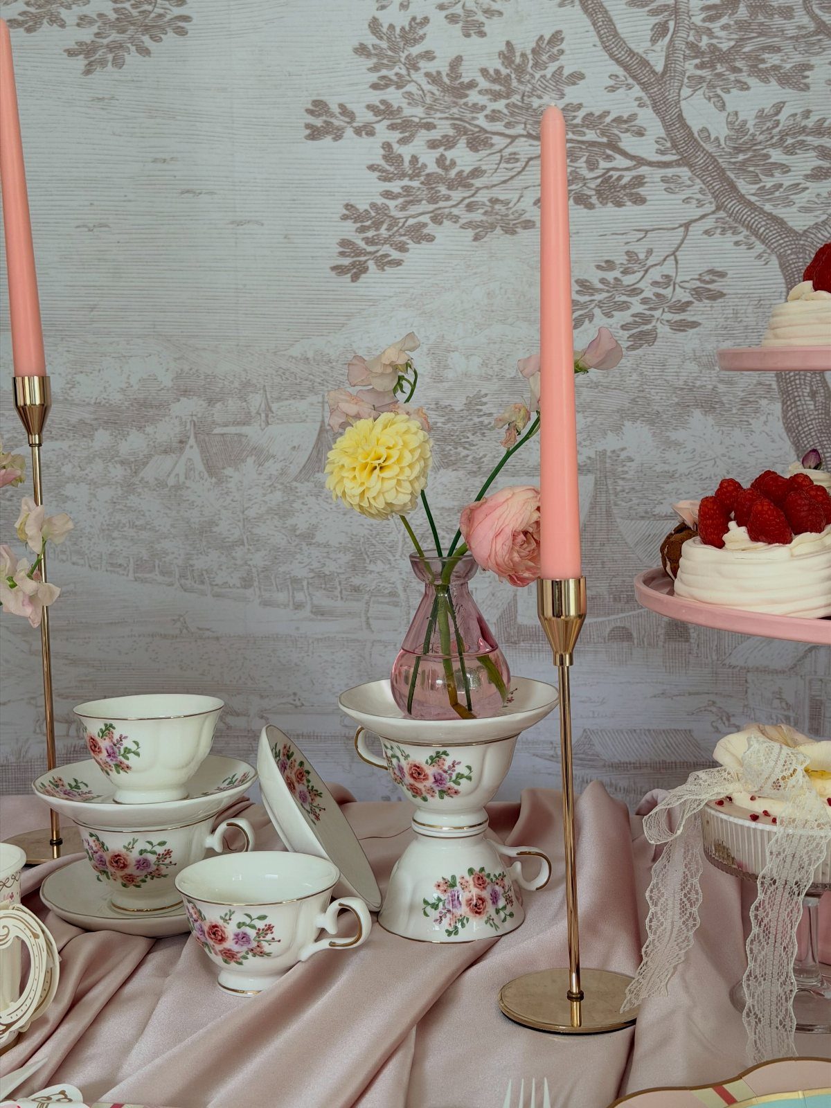 Floral porcelain teacups and pink candles arranged for an elegant vintage tea party.