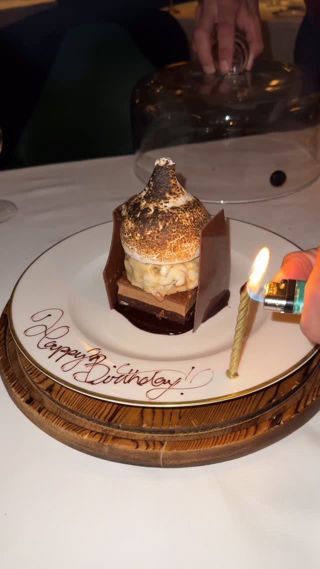 Gourmet chocolate birthday dessert with a lit gold candle on a white plate
