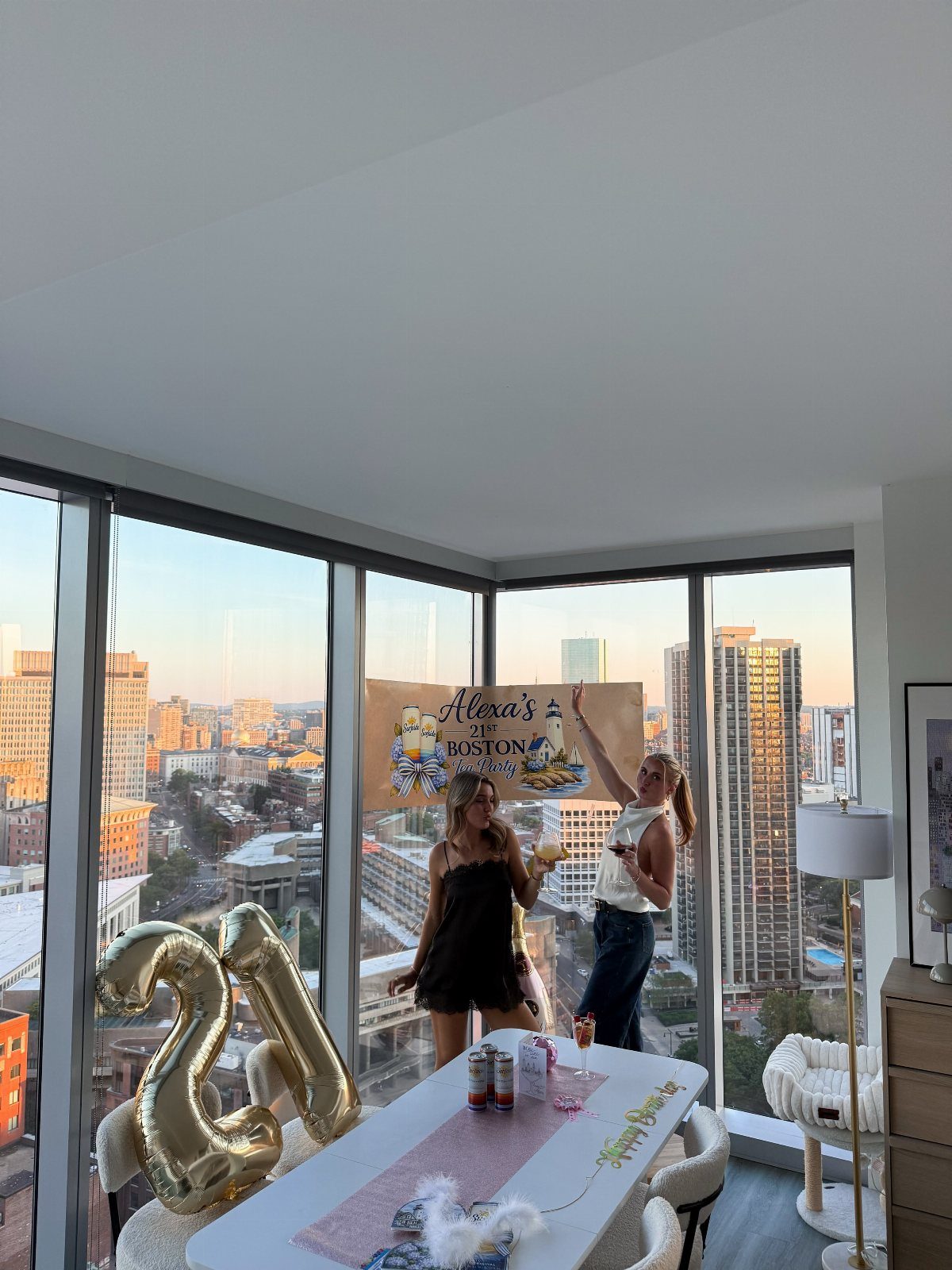 Two women celebrating a 21st birthday in a Boston apartment with gold balloons.