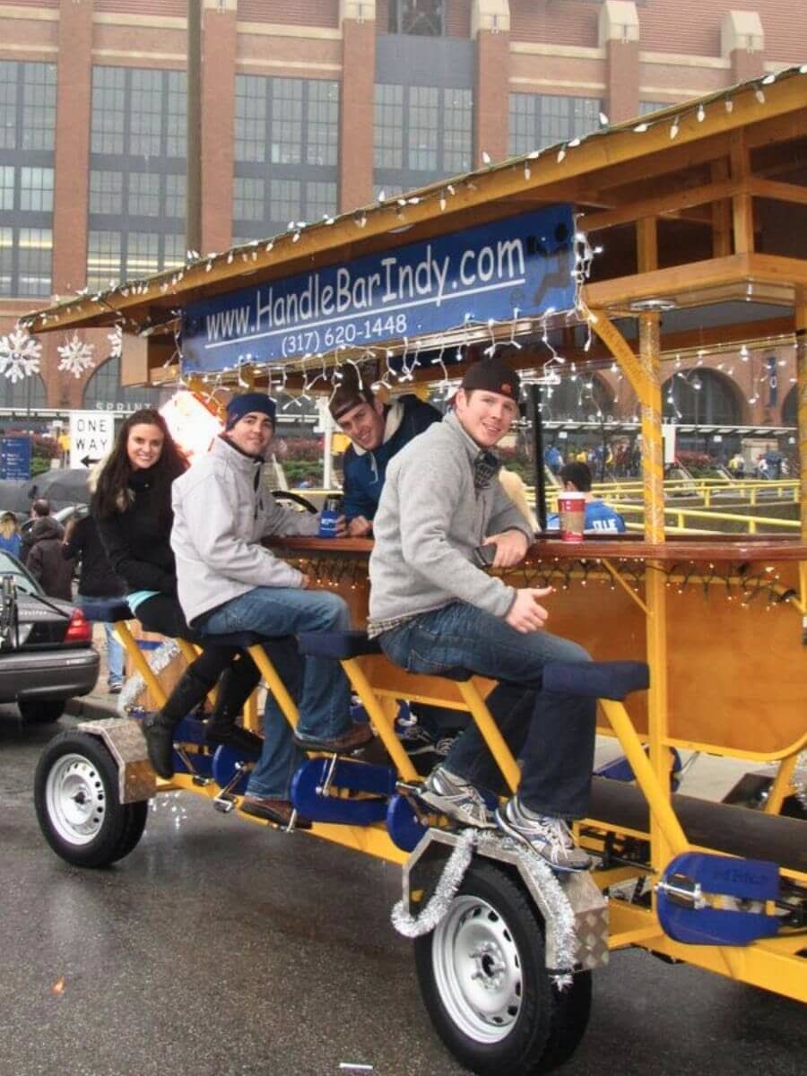 Four young adults riding a yellow pedal party bike on a city street.