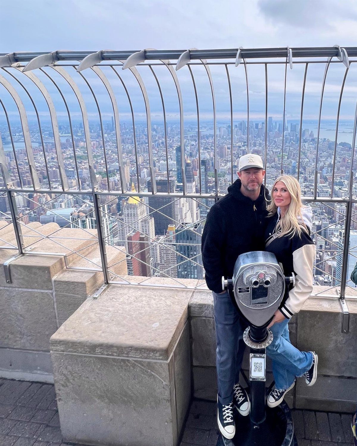 Couple posing on a city observation deck with a skyline view and telescope.