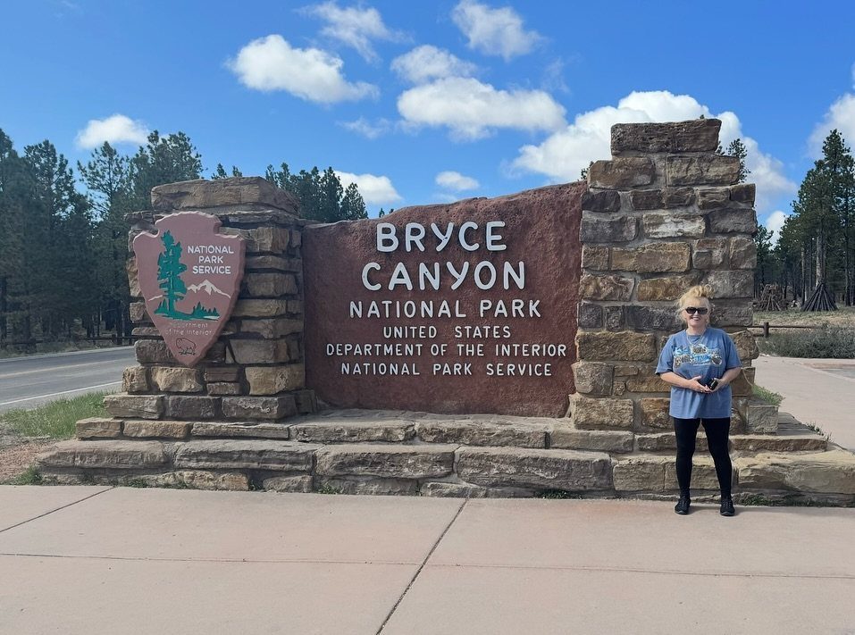 Woman standing beside the stone entrance sign of Bryce Canyon National Park.