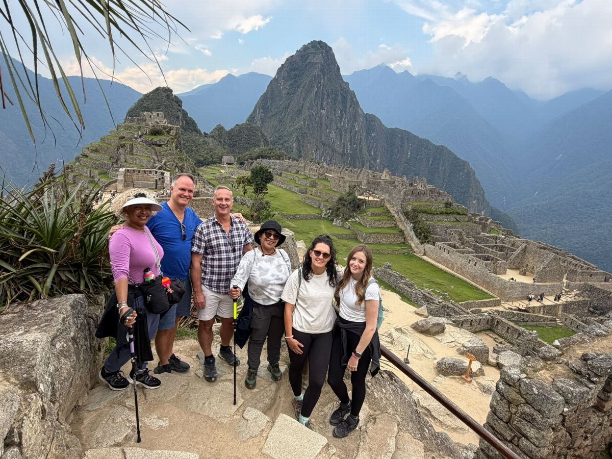 Five hikers posing on stone steps with Machu Picchu ruins and mountains behind them.
