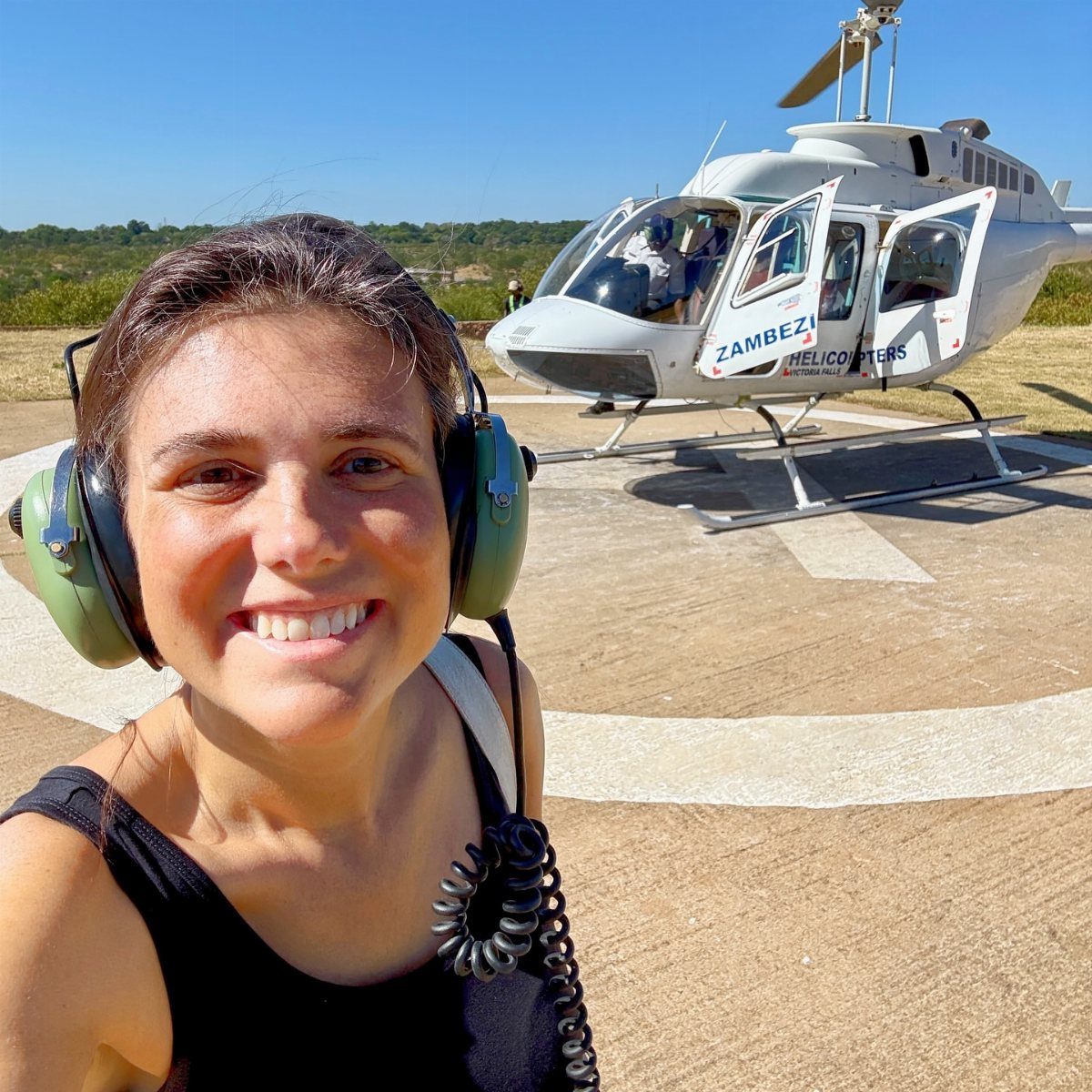 Smiling woman with aviation headsets standing in front of a white helicopter.