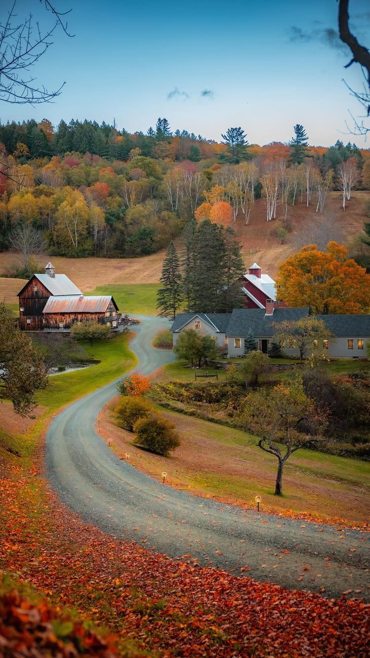 Winding gravel road through a countryside landscape with autumn trees and red barns.