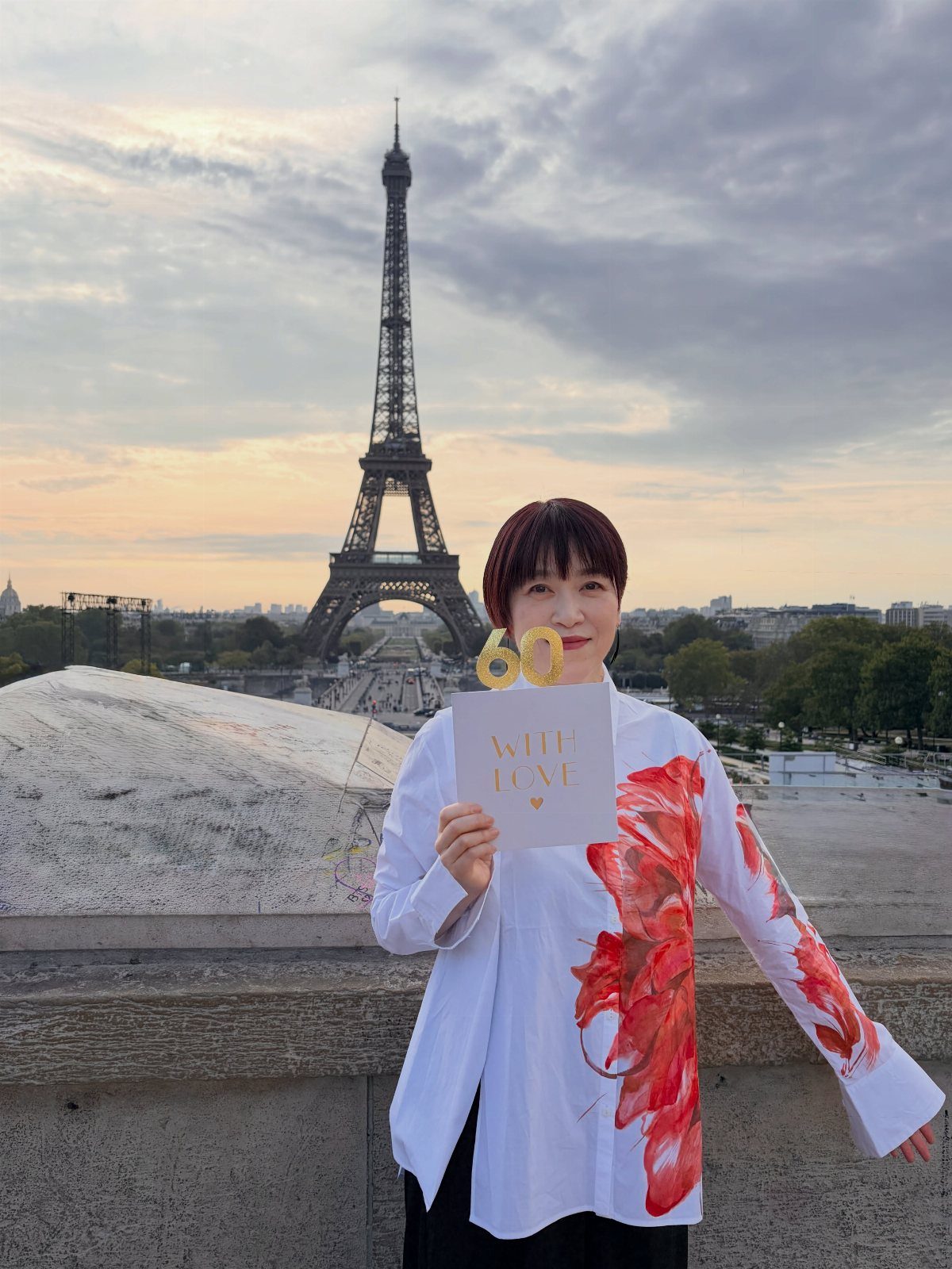 Woman holding a 60th birthday card with the Eiffel Tower in the background.