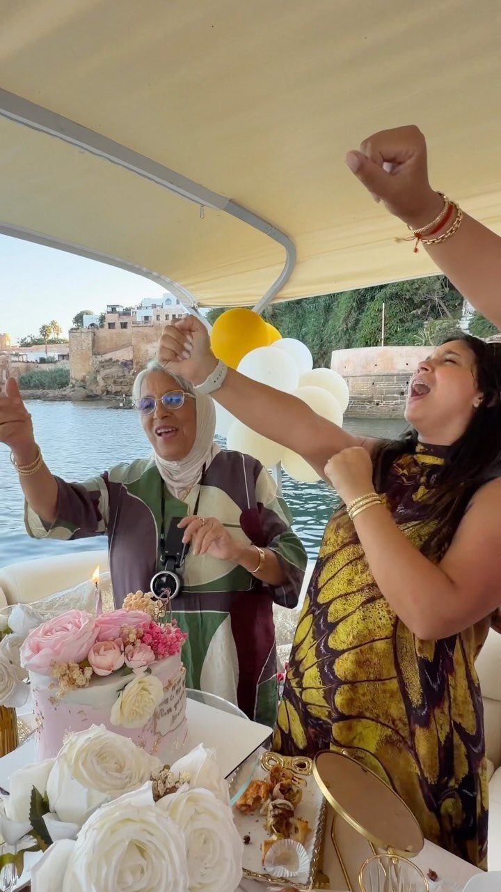 Two women celebrating with a rose cake and balloons on a boat.