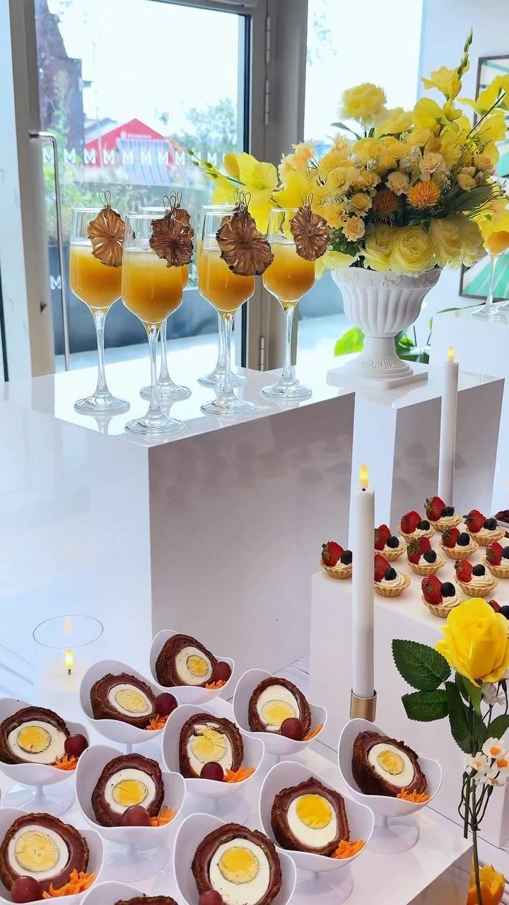 Mimosas, yellow flowers, and scotch eggs arranged on a white tiered party display.