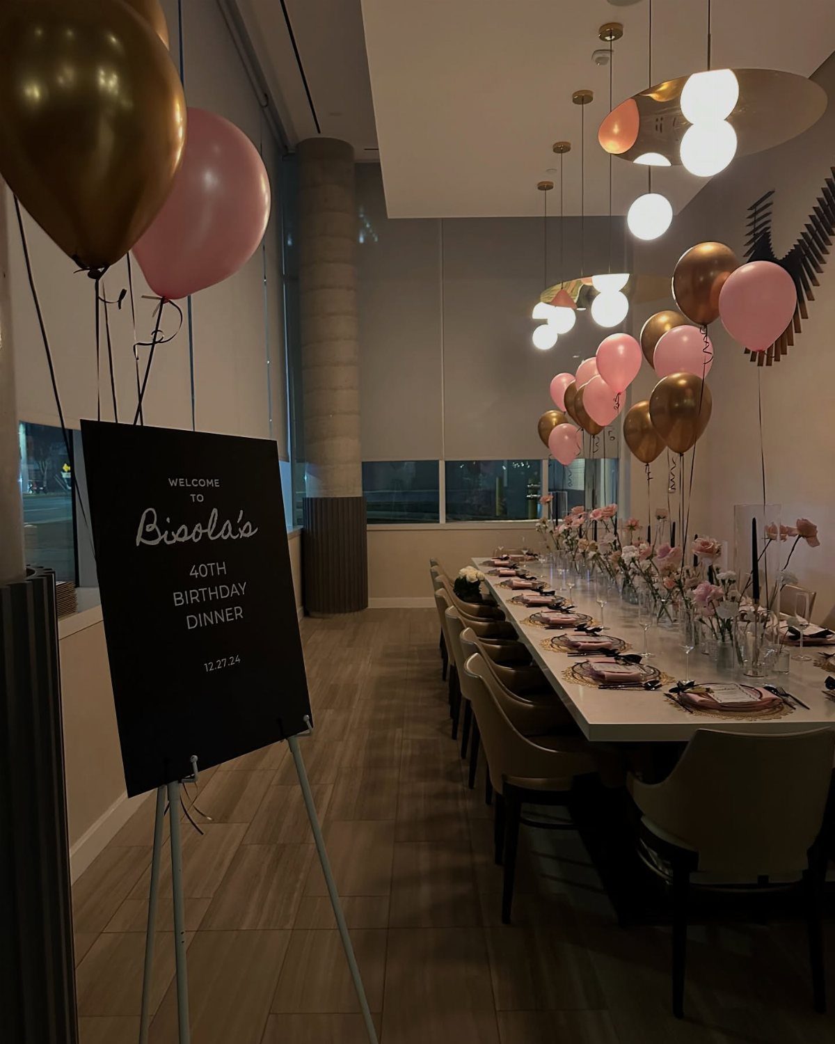 Long dining table set for a 40th birthday dinner with pink and gold balloons.