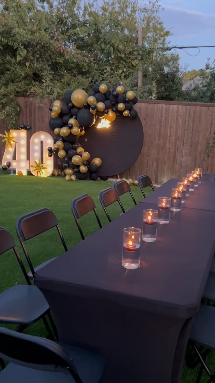 Outdoor 40th birthday party setup with black table, floating candles, and gold balloons.