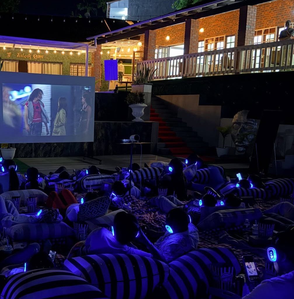 People wearing blue glowing headphones lounging on beanbags at an outdoor night cinema.