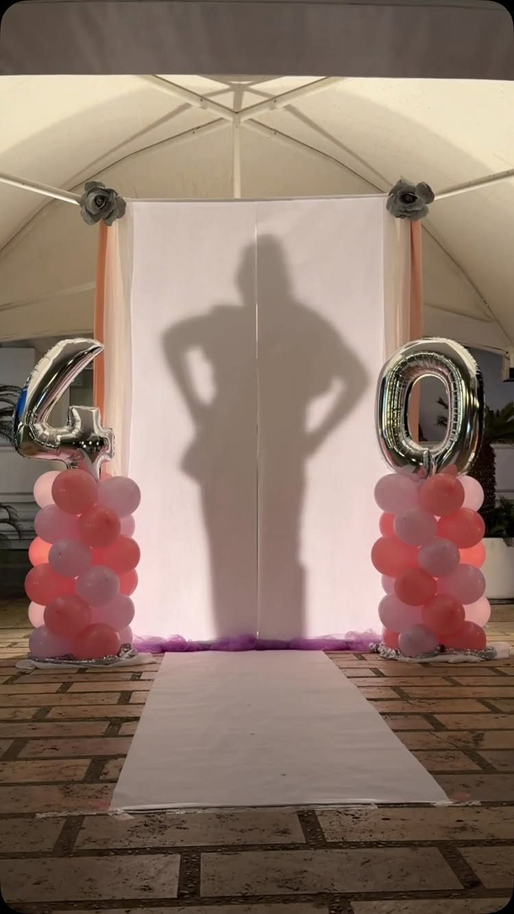 Birthday setup with silver 40 balloons, pink balloon columns, and a silhouette backdrop.