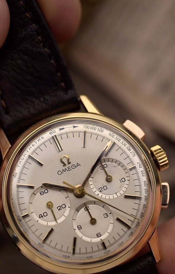 Vintage Omega chronograph watch with gold case and brown leather strap held closely.