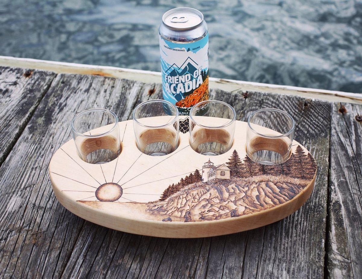Wooden beer flight paddle with four glasses and a can on a dock