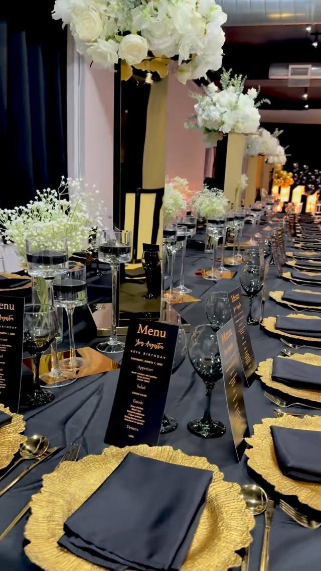 Formal banquet table setting with gold plates, black napkins, and white floral centerpieces.