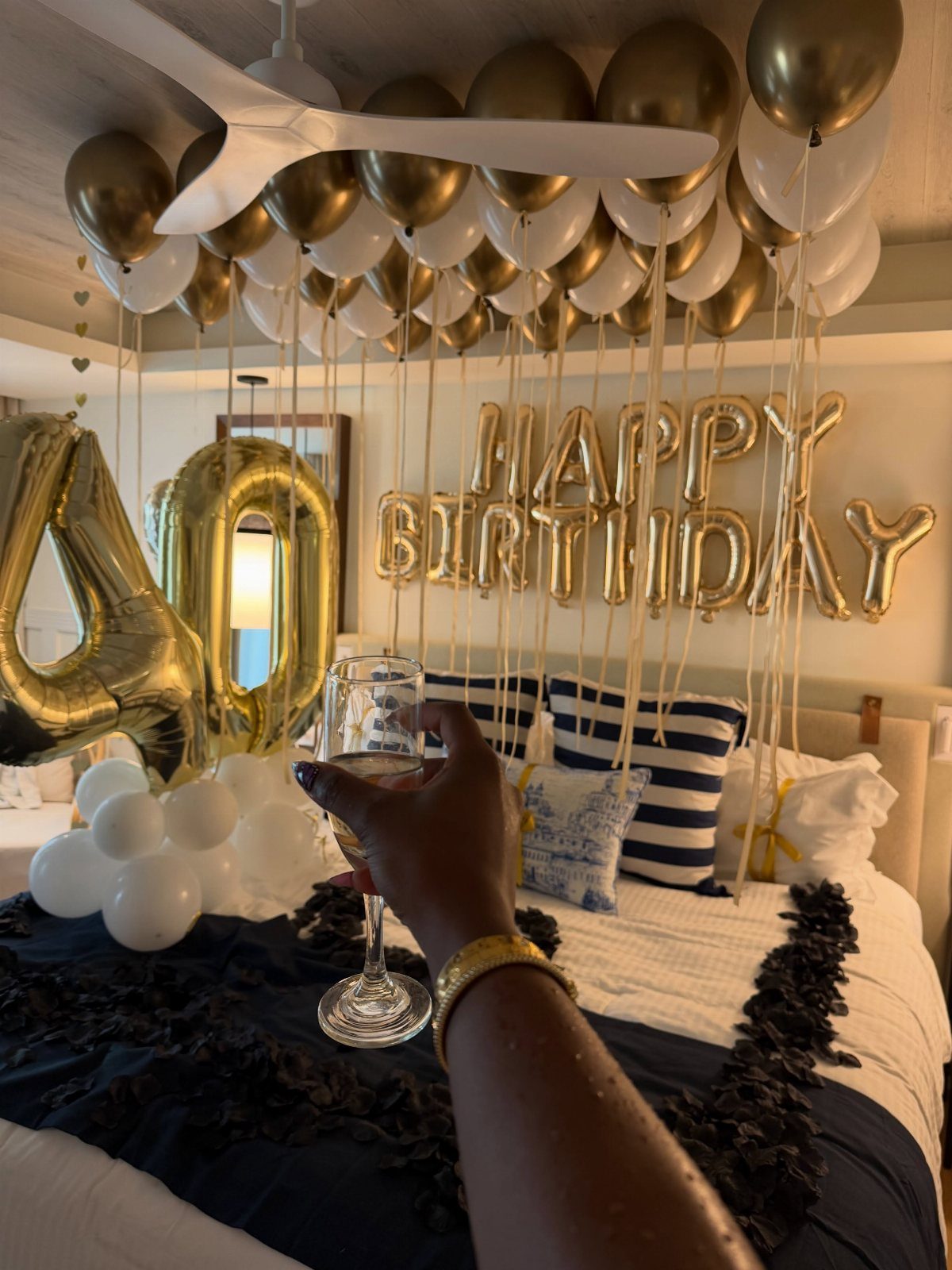 Champagne glass held in a bedroom decorated with gold 40th birthday balloons.