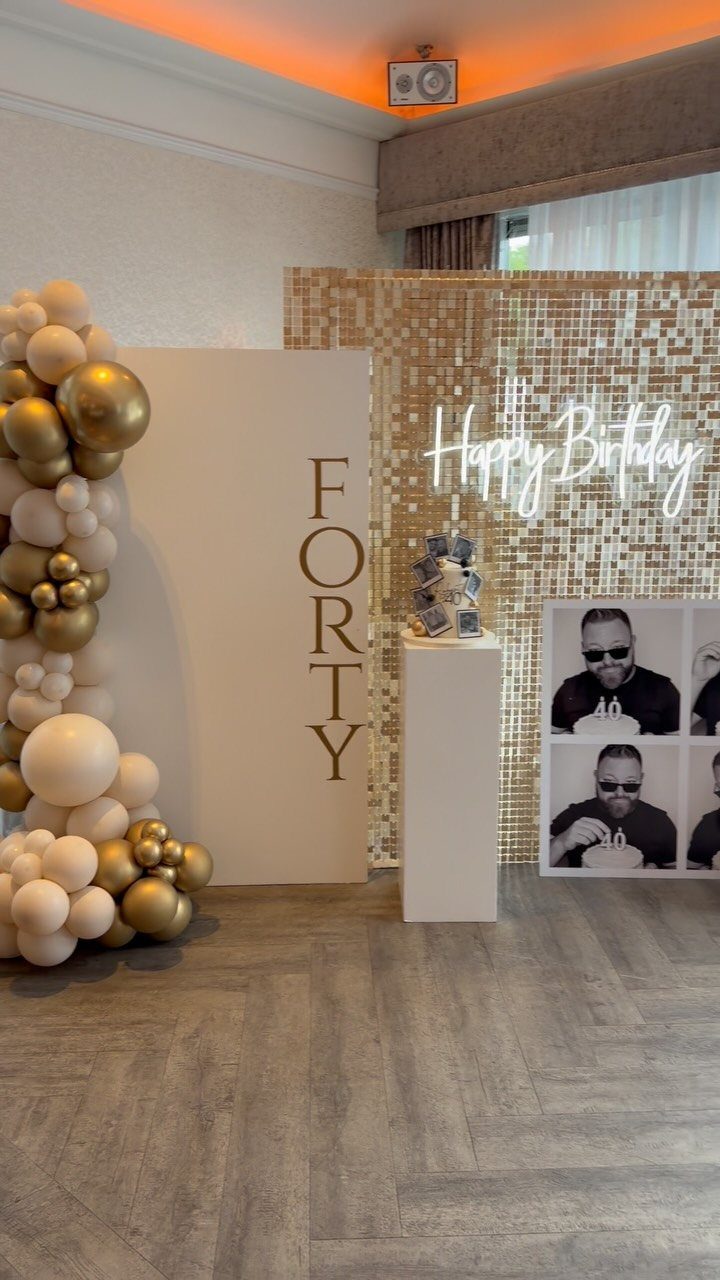 Birthday party decoration with gold balloons, a forty sign, and neon birthday lights.