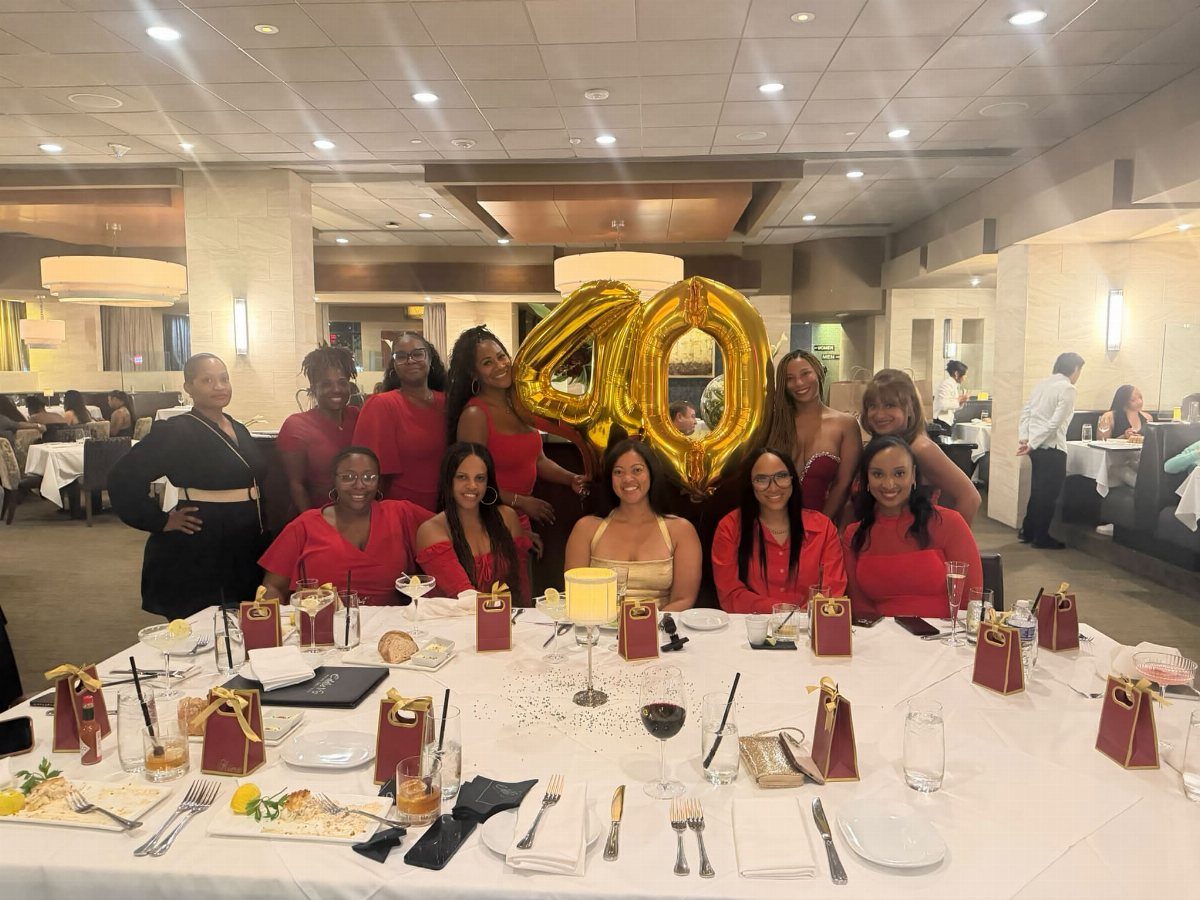 Women in red dresses posing around a dining table with gold 40 balloons.
