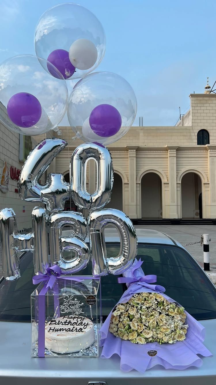 Birthday celebration setup with 40 BDAY balloons, white cake, and white rose bouquet.