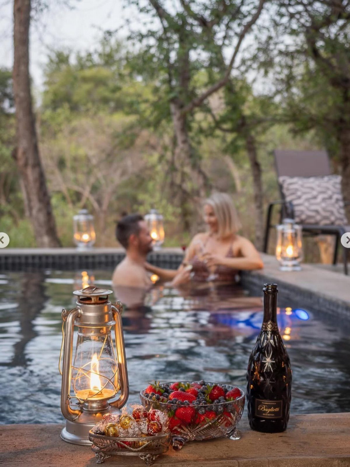 Couple relaxing in an outdoor hot tub with champagne and strawberries nearby.