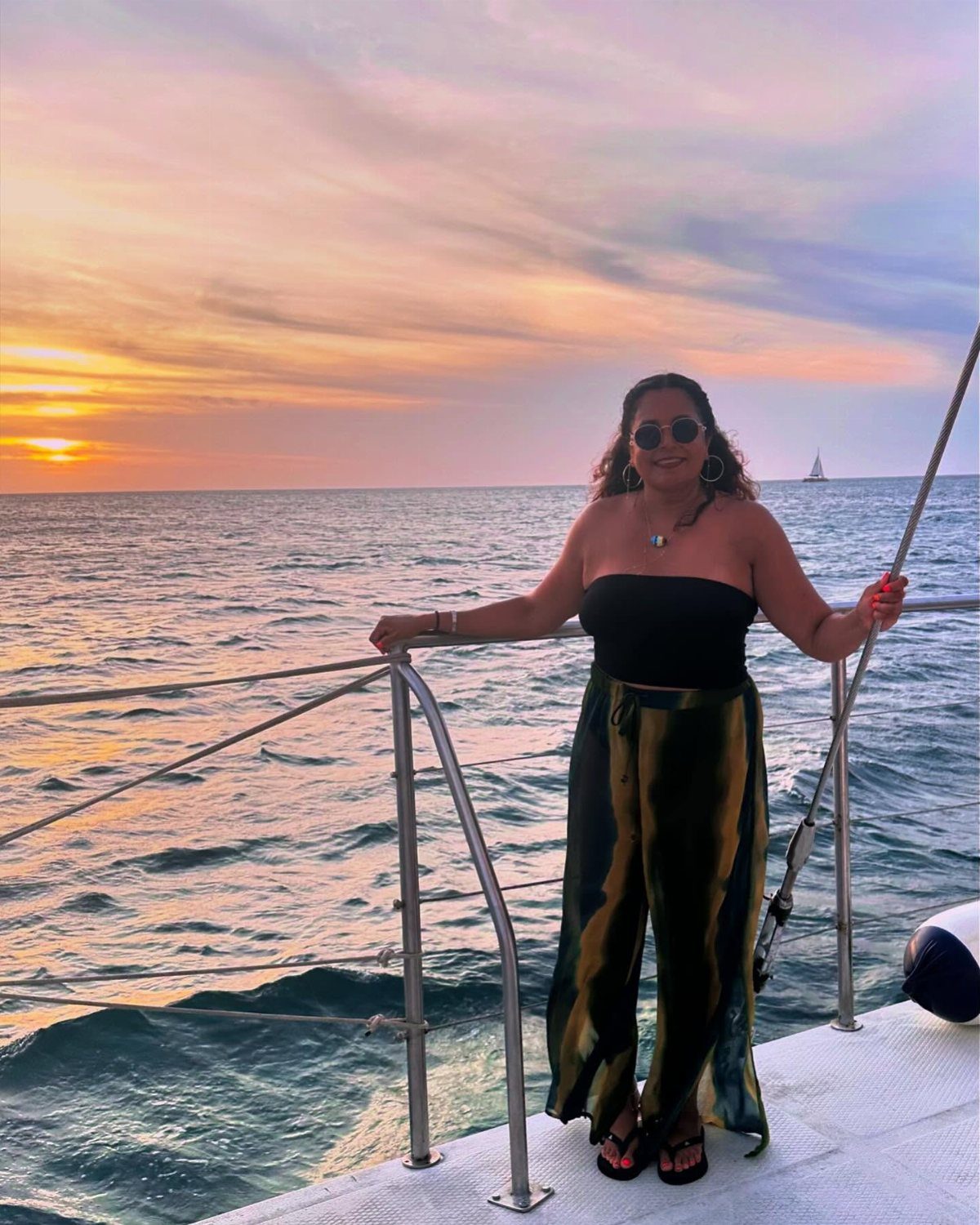 Woman standing on a boat deck during a colorful ocean sunset.
