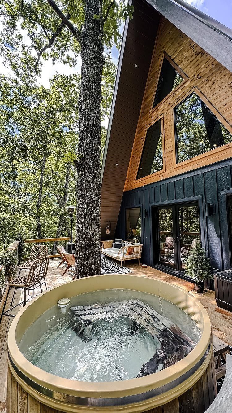 Modern A-frame cabin with an outdoor hot tub and patio surrounded by forest