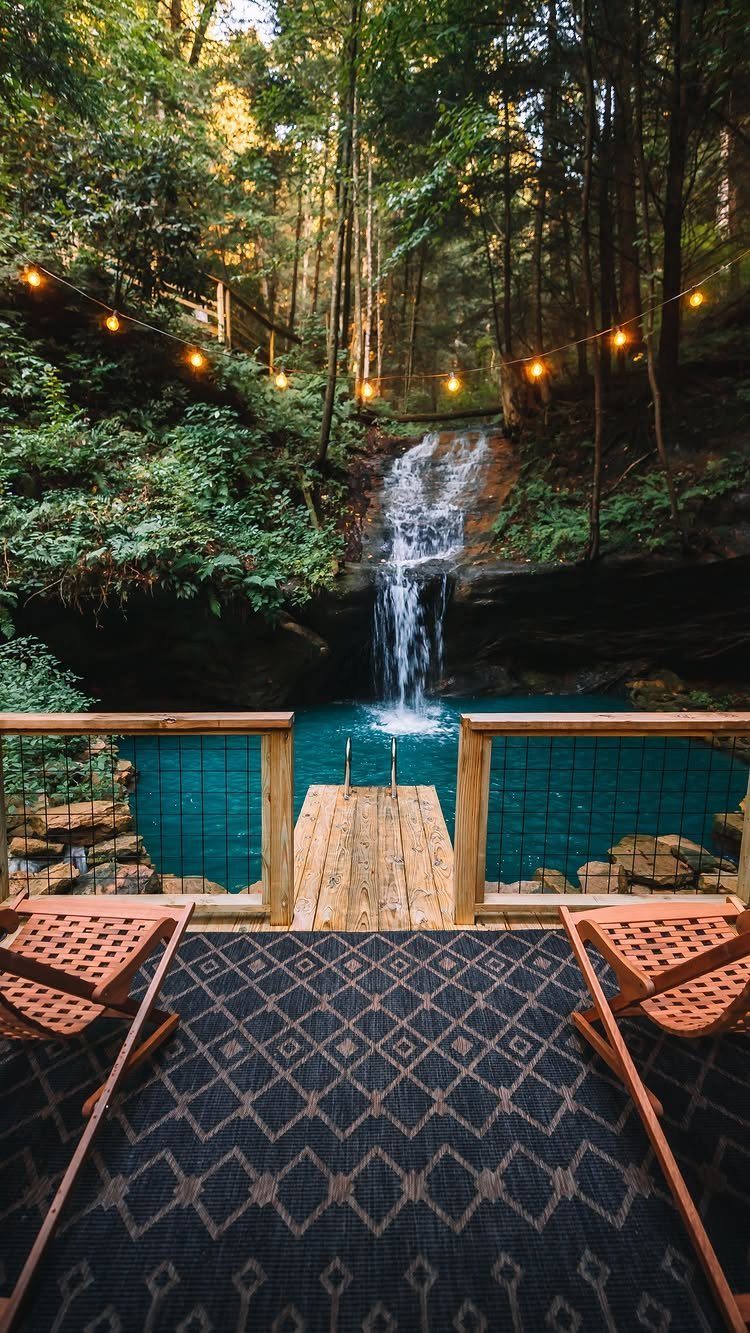 Wooden deck with lounge chairs overlooking a waterfall and turquoise pool in forest