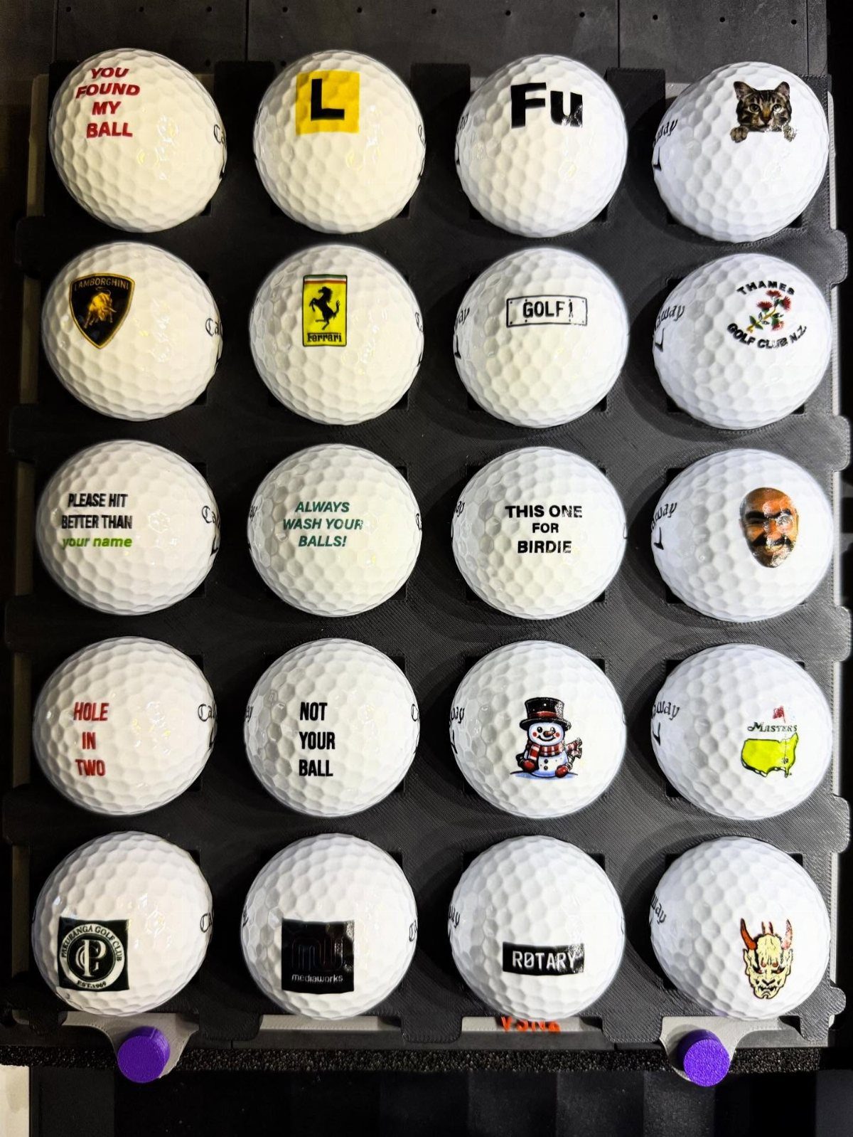 Custom printed golf balls with various logos and text on a black display rack