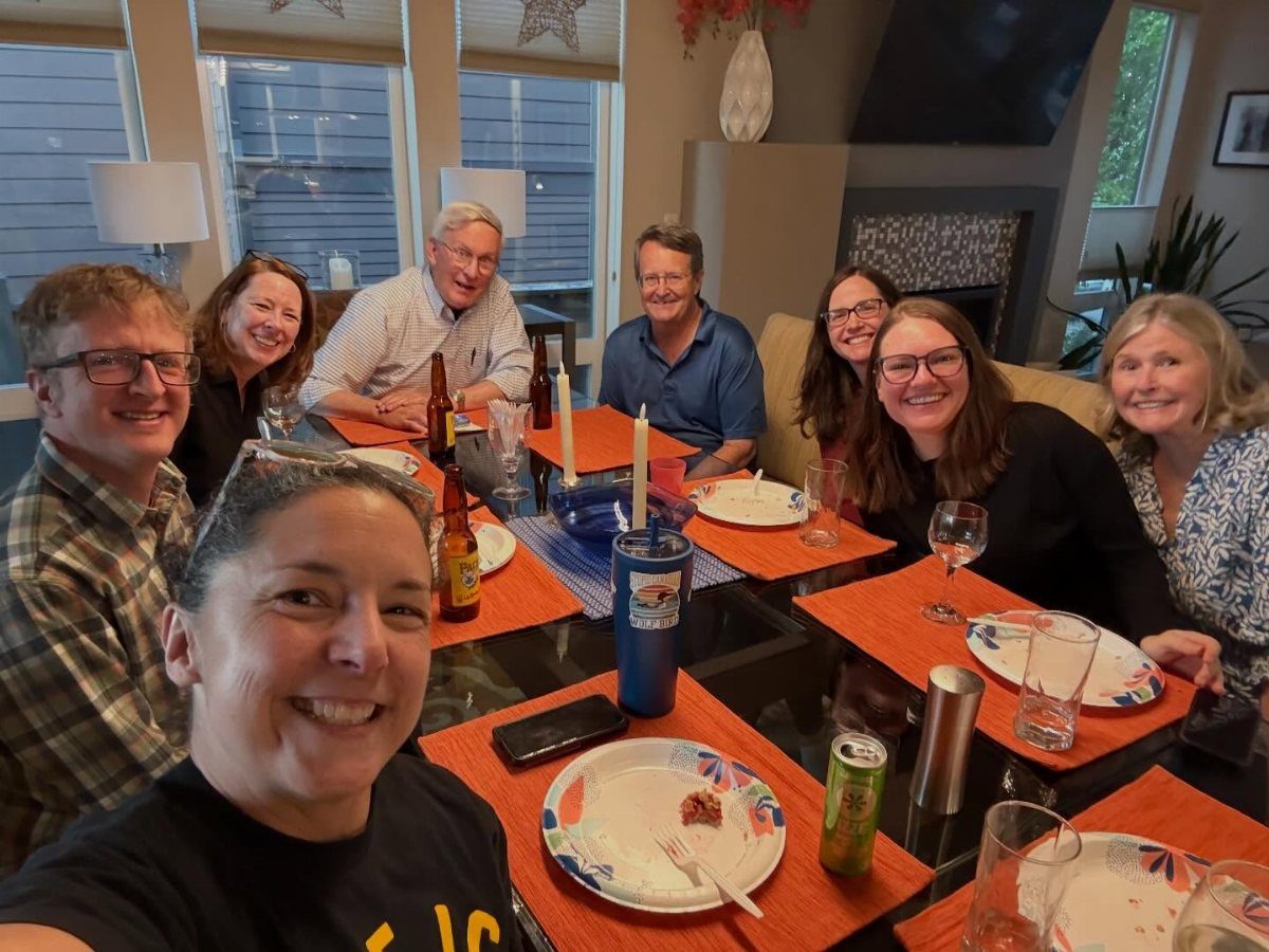 Group of smiling adults gathered around a dining table for a home dinner party.