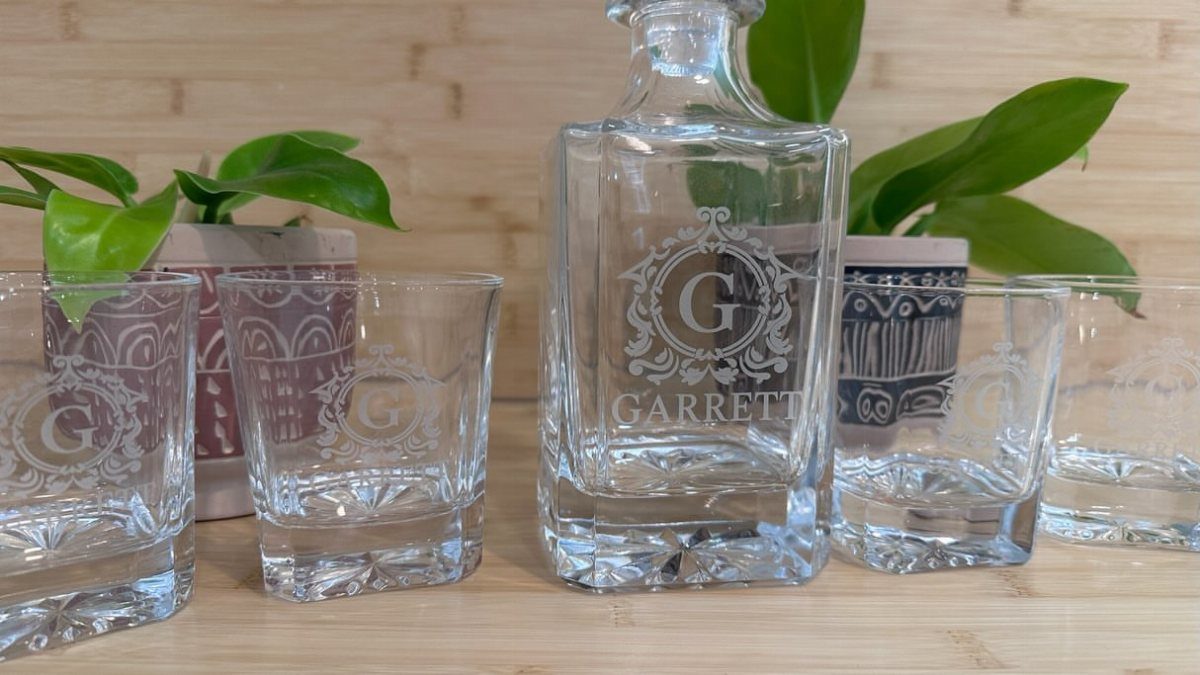 Engraved glass whiskey decanter and matching glasses with a custom monogram on wood.