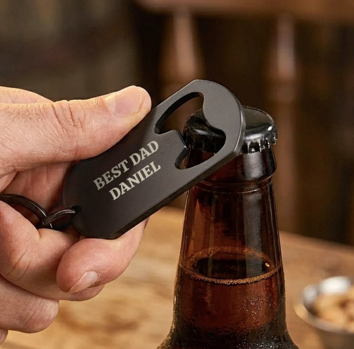Personalized black metal bottle opener opening a brown glass beer bottle.